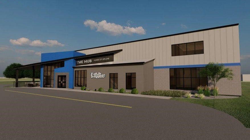 Modern, two-story building with blue and gray accents labeled THE HUB and HOME OF ONLINE on the facade; landscaped with shrubs and plants, under a clear blue sky—a fitting space for public relations and tracking social media trends.