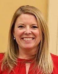 A woman with straight, blonde hair wearing a red top smiles at the camera against a beige background, embodying the confidence of a Philly PR Girl skilled in public relations.