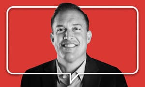 A smiling man in a suit is centered against a solid red background, with a white outline of a speech bubble around him, reflecting modern public relations in today’s dynamic news media landscape.