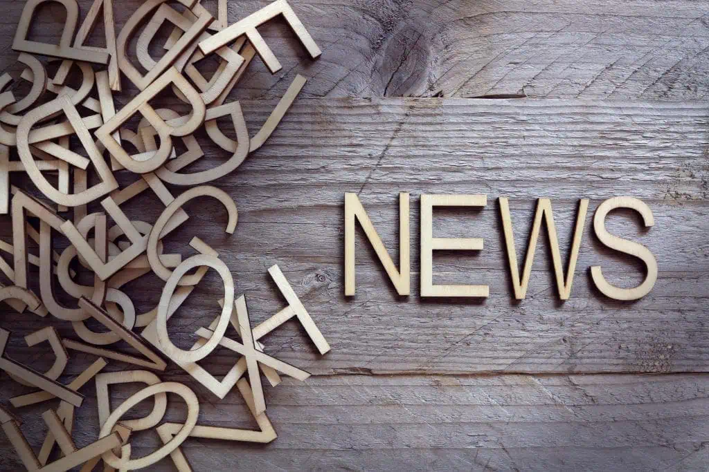 Wooden letters are scattered on the left side of a wooden surface, with the word NEWS—perfect for marketing or keeping up with social media trends—neatly arranged on the right side.
