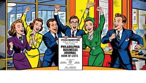 A group of five cheerful businesspeople in colorful suits celebrate around a large certificate for Sylvia Marketing’s inclusion in the Philadelphia Business Journal Book of Lists, highlighting their expertise in social media trends, in a vibrant office setting.