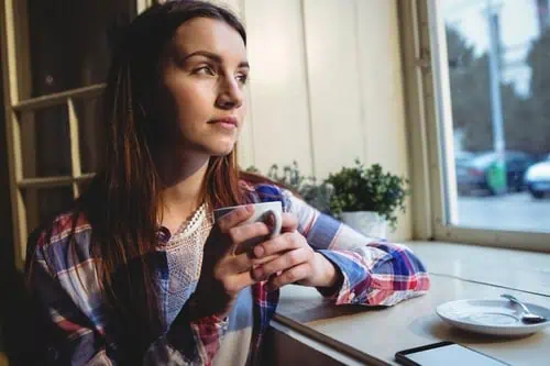 Young woman holding a coffee mug, contemplating by a window, symbolizing career opportunities in pub.