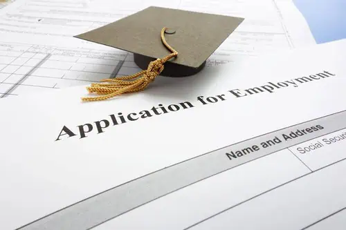 Graduation cap placed on an employment application form, symbolizing career opportunities.