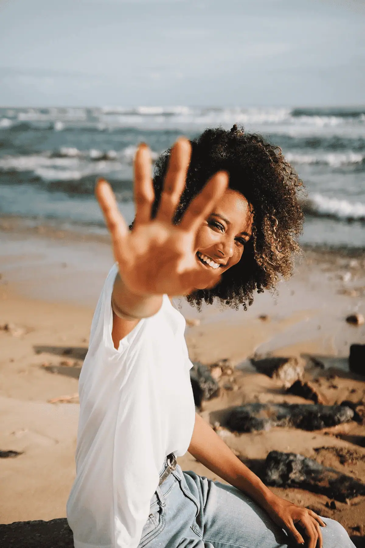 Woman at the beach waving with a bright smile, showcasing joyful public relations and marketing vibe.